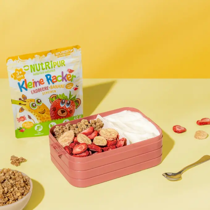Bild zeigt die kleinen Racker der Sorte Erdbeere und Banane von Nutripur mit Joghurt und Flakes als Schulsnack in einer Brotdose