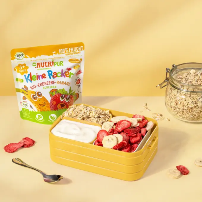 Bild zeigt die kleinen Racker der Sorte Bio-Erdbeere und Banane von NutriPur mit Verpackung und Brotdose